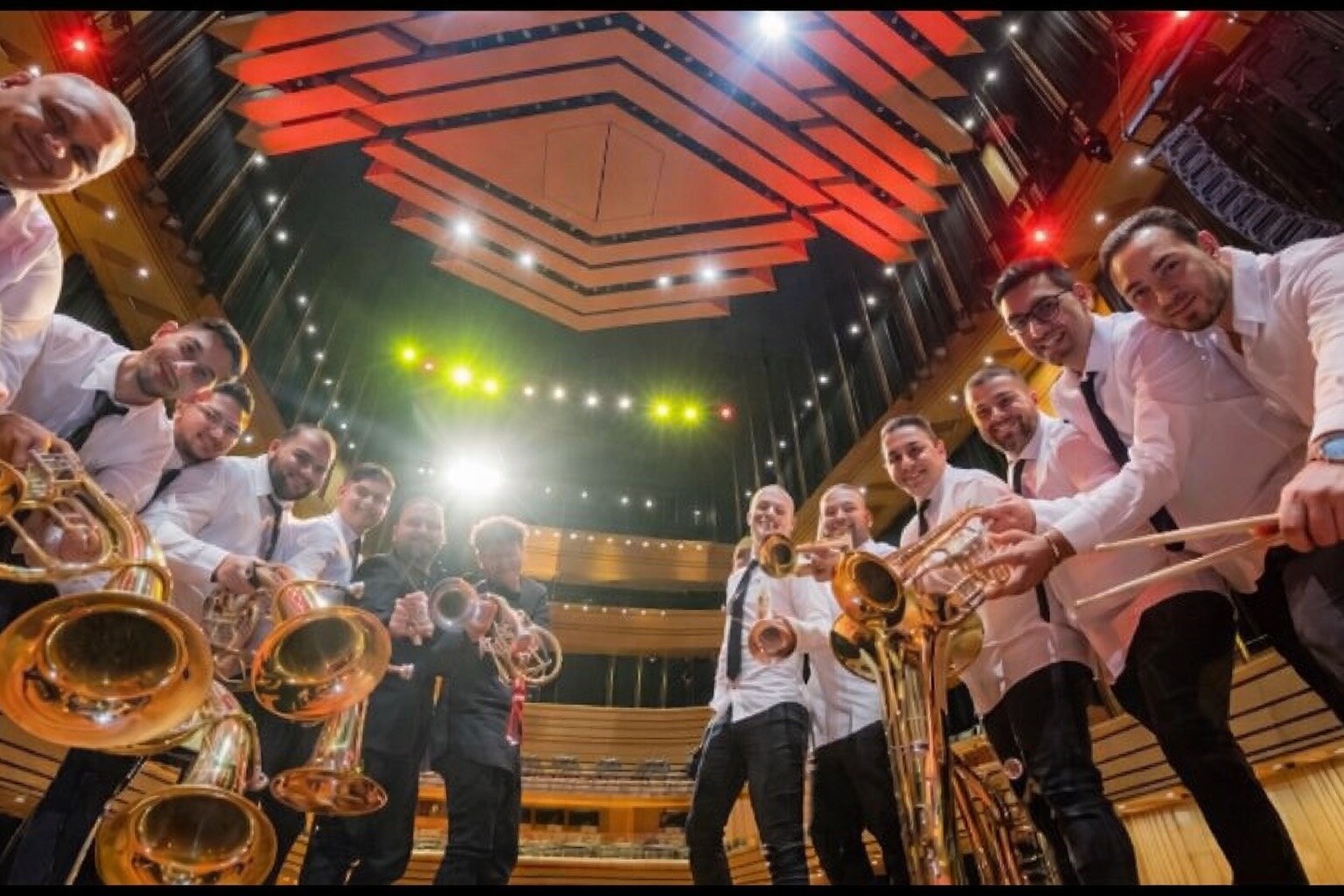 Orkestar u belim košuljama snimljen odozdo u koncertnoj dvorani